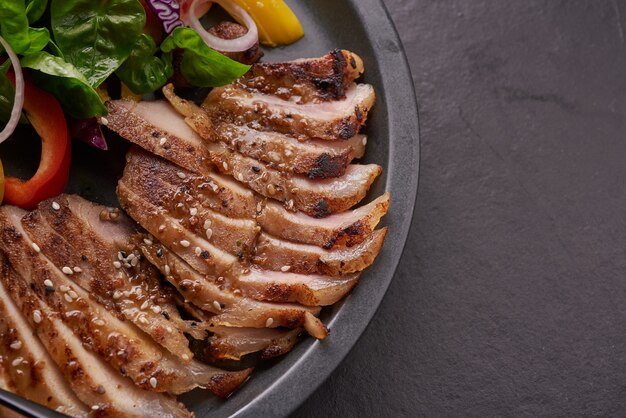 Gegrilltes Steak mit frischem Gemüse, Paprika, Tomaten, roten Zwiebeln, rosa Pfeffer und Gewürzen. Hausgemachtes leckeres Essen. Konzept für leckeres und gesundes Essen. Schwarze Steinoberfläche. Schweinesteak mit Salat