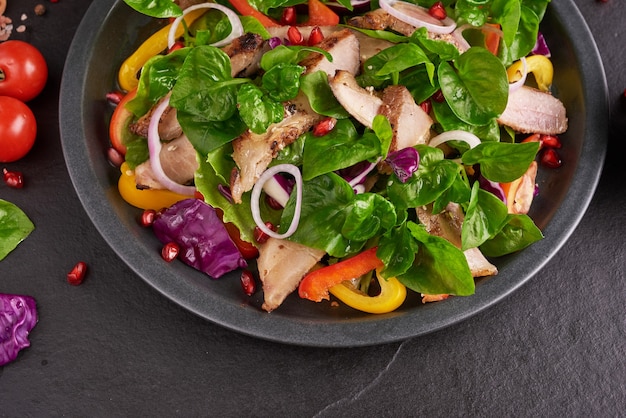 Gegrilltes Steak mit frischem Gemüse, Paprika, Tomaten, roten Zwiebeln, rosa Pfeffer und Gewürzen. Hausgemachtes leckeres Essen. Konzept für leckeres und gesundes Essen. Schwarze Steinoberfläche. Schweinesteak mit Salat