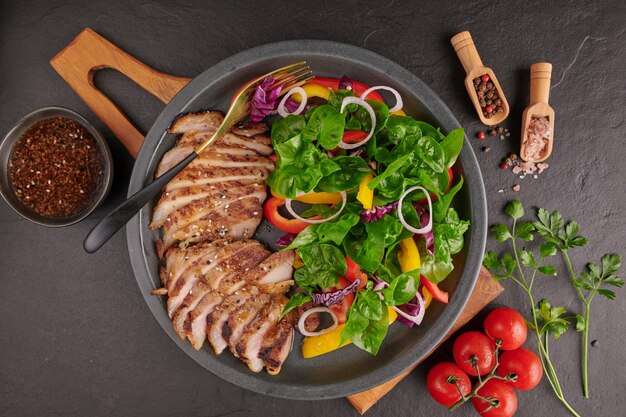 Gegrilltes Steak mit frischem Gemüse, Paprika, Tomaten, roten Zwiebeln, rosa Pfeffer und Gewürzen. Hausgemachtes leckeres Essen. Konzept für leckeres und gesundes Essen. Schwarze Steinoberfläche. Schweinesteak mit Salat