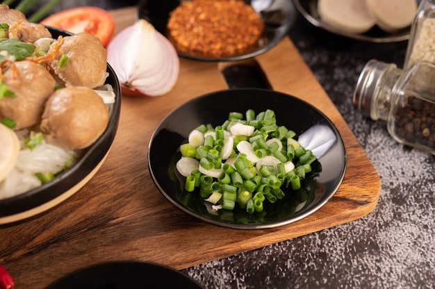 Gehackte Frühlingszwiebeln auf einem schwarzen Teller mit Chili, Tomaten und Knoblauch