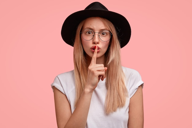 Kostenloses Foto geheime schöne süße junge frau mit langen blonden haaren, macht schweigegeste, hat die absicht, etwas zu tun, von dem niemand etwas wissen sollte