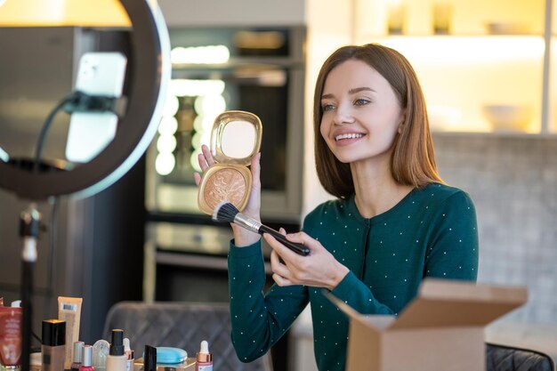 Geheimnisse guten Make-ups. Hübsche junge Frau im grünen Kleid, das Make-up-Tipps zeigt