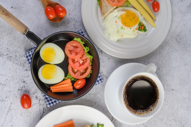 Gekochte Eier, Karotten und Tomaten in einer Pfanne mit Tomaten auf einem Holzlöffel und einer Kaffeetasse.