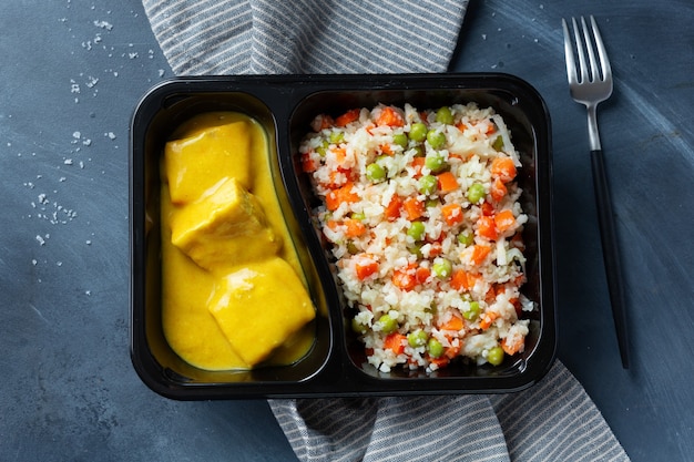 Gekochte Fischstücke mit rohem Gemüse und Currysauce, serviert in einer Lunchbox. Nahaufnahme.