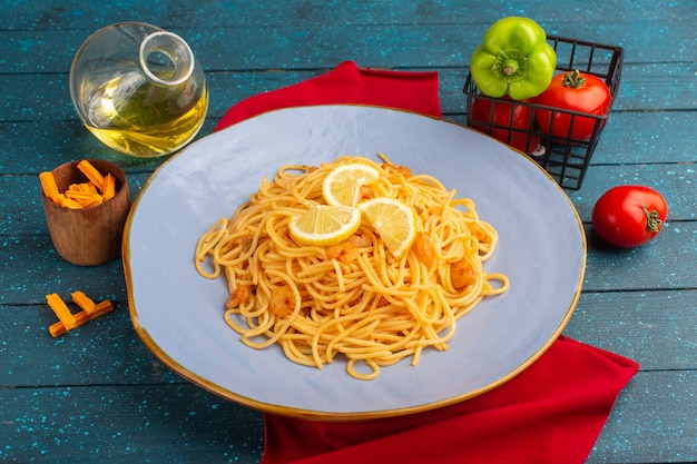 gekochte italienische Pasta mit Zitronenscheiben in blauem Teller mit Öl und Gemüse auf blau