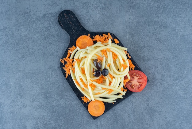 Gekochte Spaghetti mit Gemüse auf schwarzem Brett.