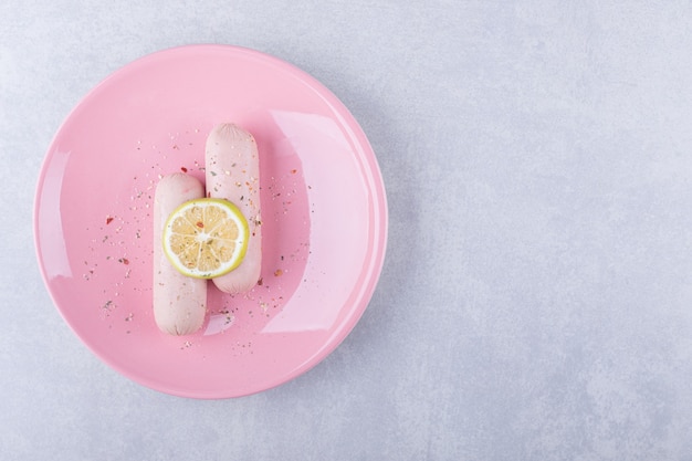 Gekochte Würste mit Zitrone auf rosa Teller dekoriert.k