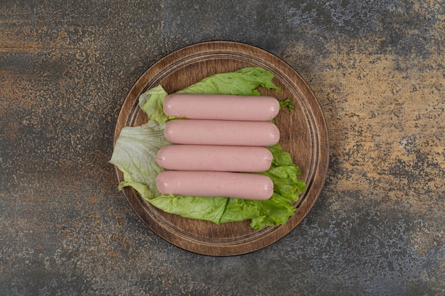 Gekochte Würste und Salat auf Holzbrett.