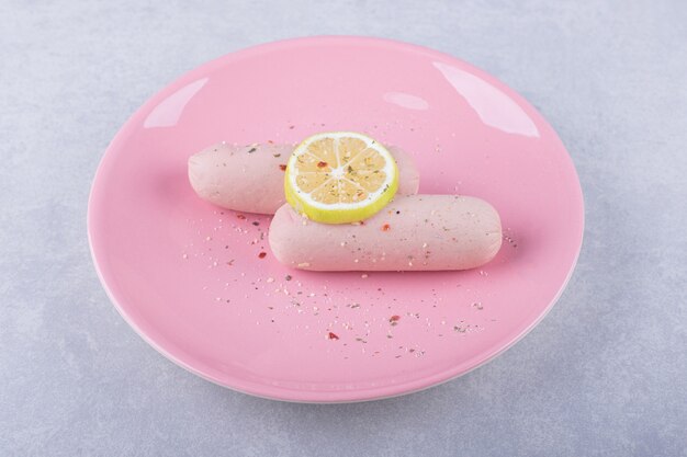 Gekochte Würste verziert mit Zitrone auf rosa Teller. k