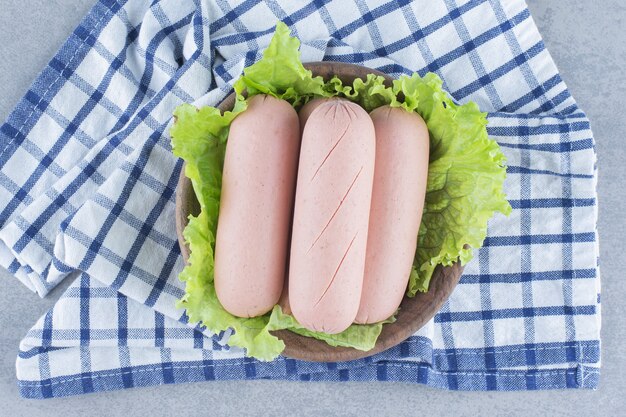 Gekochte Wurst auf Holzschale mit Salatblatt.