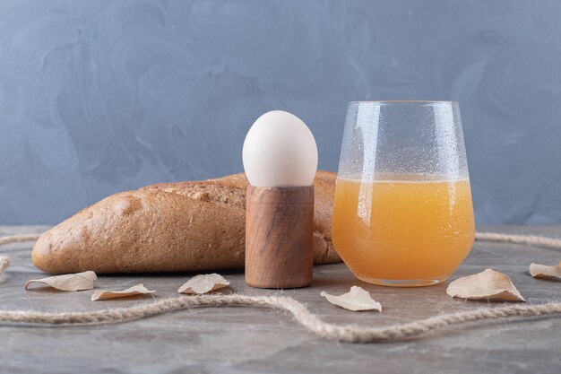 Gekochtes Ei, Brot und ein Glas Saft auf Marmortisch.