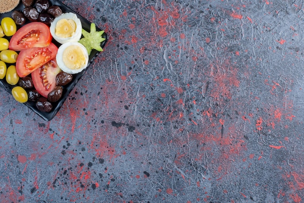 Gekochtes ei mit schwarzen und grünen marinierten oliven und tomaten.