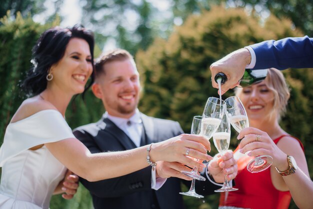 Gelächeltes Hochzeitspaar mit besten Freunden trinkt Champagner im Freien und lächelt