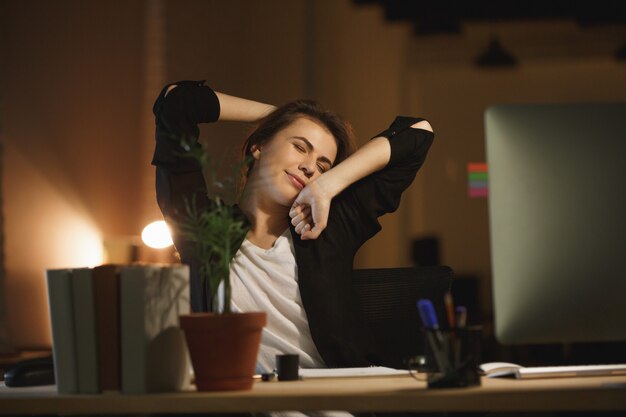 Gelangweilte junge Frau, die nachts im Büro sitzt