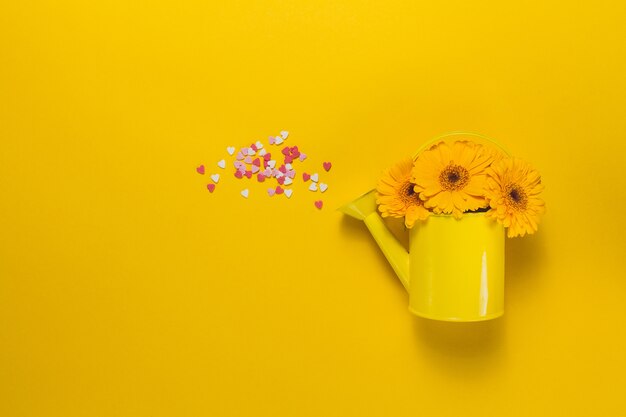Gelbe Gießkanne mit Blumen und Herzen Konfetti