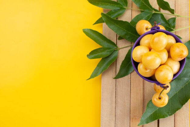 Gelbe Kirschen der Draufsicht weich und saftig im lila Korb auf gelbem Schreibtisch, Fruchtsommerfarbe
