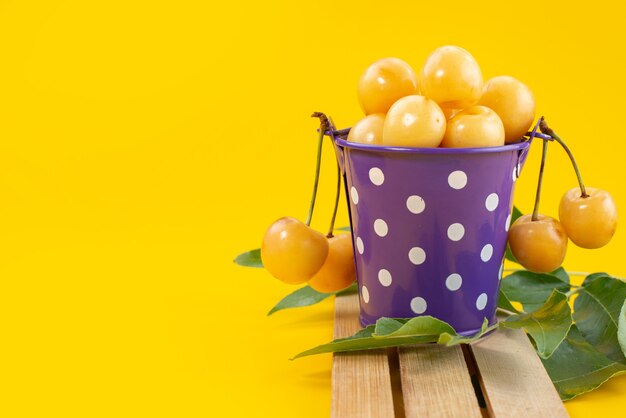 Gelbe Kirschen der Vorderansicht, die innerhalb des purpurroten Korbs auf hölzernem Schreibtisch und gelbem Fruchtfarbsommer weich und süß sind