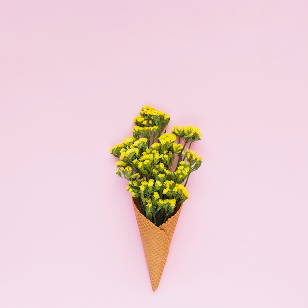 Gelbe kleine Blumen innerhalb des Waffelkegels gegen rosa Hintergrund