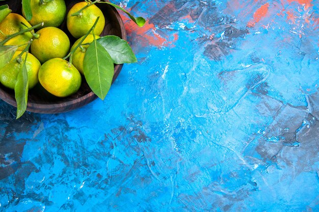 Gelbe Mandarinen der Draufsicht mit Blättern in der Holzschale auf blauer Oberfläche mit Kopienraum