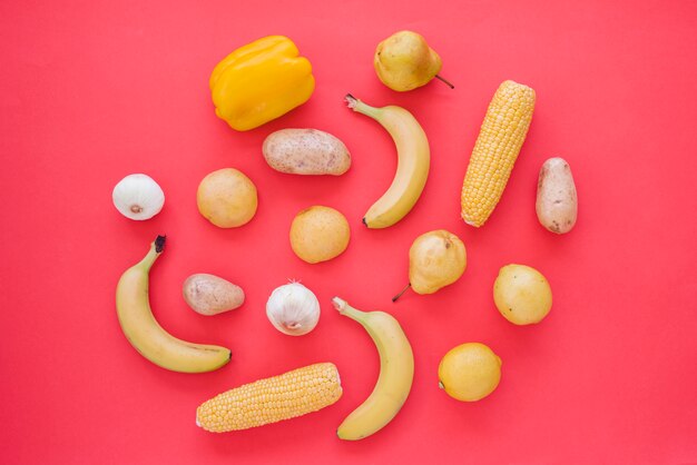Gelbe Paprika; Zwiebel; Kartoffel; Birnen; Limette; Mais und Knoblauch auf rotem Hintergrund