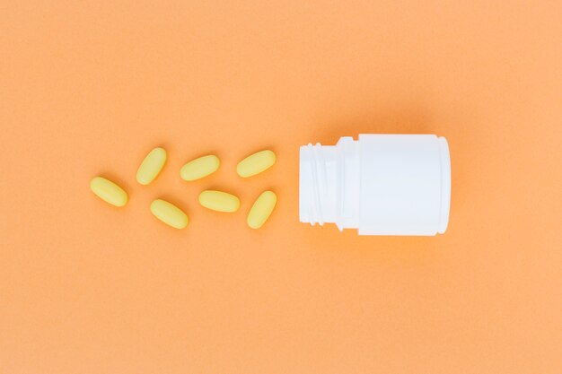 Gelbe Pillen liefen weiße Plastikflasche auf einem orange Hintergrund über