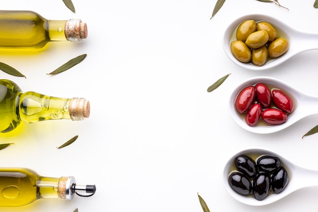 Gelbe rote schwarze Oliven in den Löffeln mit Blättern und Ölflaschen