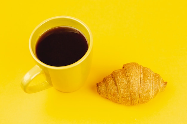 Gelbe Schale mit Kaffee und Hörnchen auf einem gelben Hintergrund