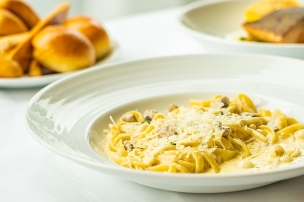 Gelbe Spaghetti Carbonara mit weißer Sahnesauce im Teller auf Tisch - italienischer Essensstil