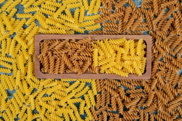 Gelbe und braune rohe Fusilli-Nudeln auf Holzplatte.