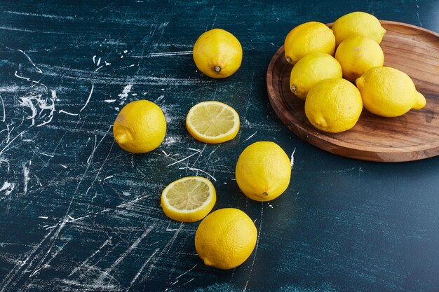 Gelbe Zitrone und Scheiben auf blauem Hintergrund in einer hölzernen Platte.