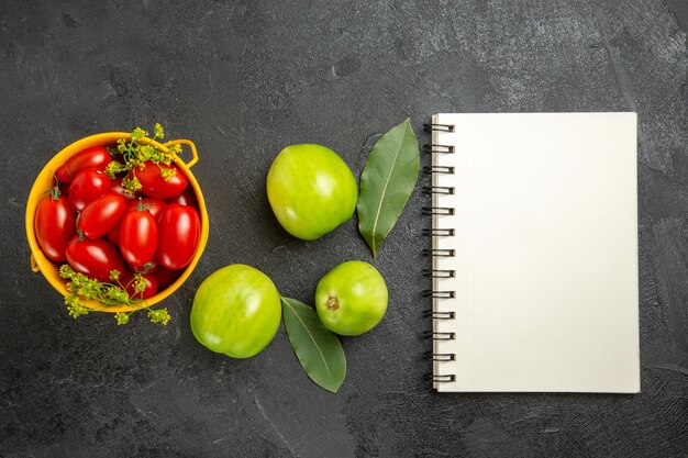 Gelber Eimer der Draufsicht gefüllt mit Kirschtomaten und Dillblumen Lorbeerblätter grüne Tomaten und ein Notizbuch auf dunklem Grund mit Kopierraum