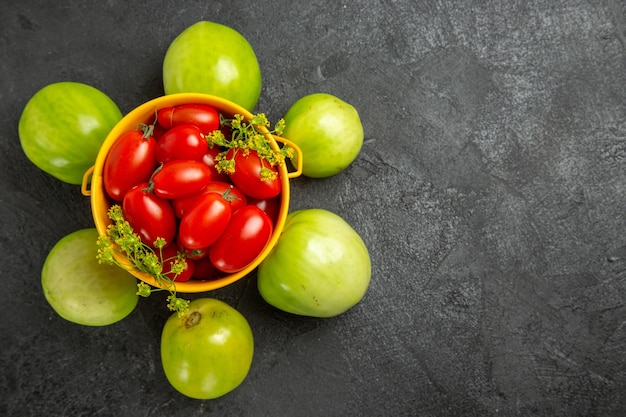 Gelber Eimer der Draufsicht gefüllt mit Kirschtomaten und Dillblumen und abgerundet mit grünen Tomaten auf dunkler Oberfläche