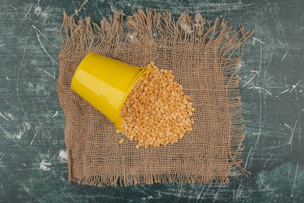 Gelber Eimer mit Weizen auf Sackleinen auf Marmoroberfläche