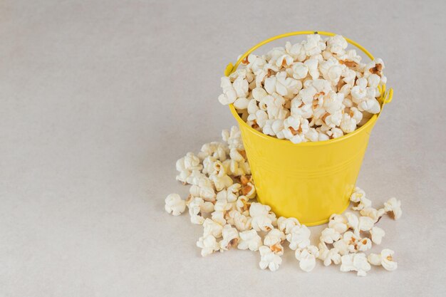 Gelber Eimer übermäßig gefüllt mit knusprigem Popcorn auf Marmortisch.