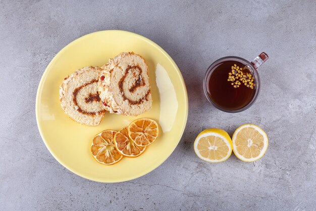 Gelber Teller mit geschnittenem Rollkuchen und Tasse Tee auf Steinoberfläche.