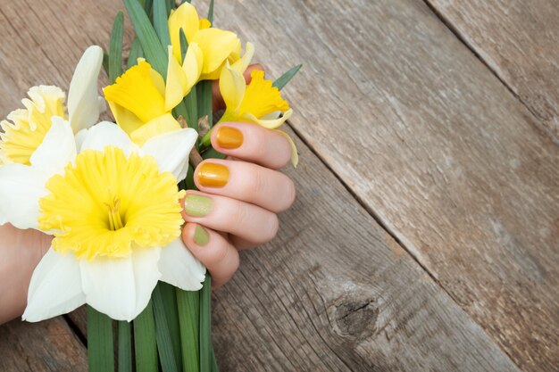 Gelbes Nageldesign. Weibliche Hand mit Glitzer-Maniküre, die Narzissenblüten hält.