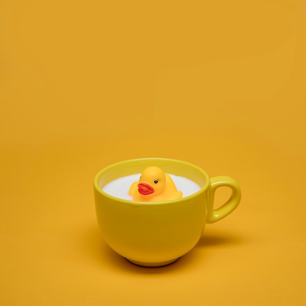 Gelbes Stillleben der Badeente in der Tasse Milch