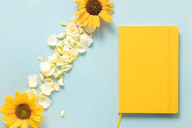 Gelbes Tagebuch nahe Sonnenblumen und Blumenblättern über blauem Hintergrund