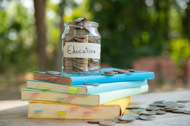 Geldmünzen sparen in Glasflasche für Konzeptinvestitionsfondsfinanzierung und -geschäft, platziert auf dem Lehrbuch. Inhalt Geld sparen für Bildung.