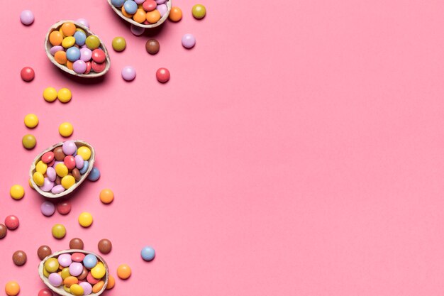 Gem-Süßigkeiten in den defekten Schokoladen-Ostereiern auf rosa Hintergrund