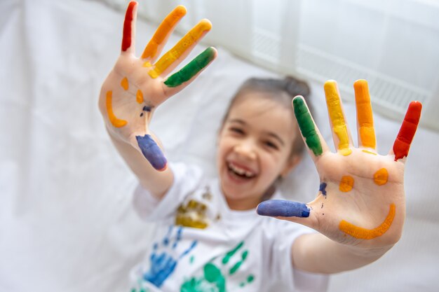 Gemaltes Lächeln auf den Handflächen eines kleinen Mädchens. Lustige helle Zeichnungen auf Kinderpalmen.