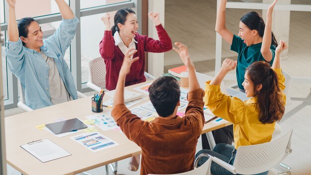 Gemischtrassige Gruppe junger kreativer Leute in der intelligenten Freizeitkleidung, die Geschäftsgestenhand hoch fünf bespricht, zusammen lachend und lächelnd im Brainstorming-Treffen im Büro. Teamwork-Konzept für Mitarbeiter.