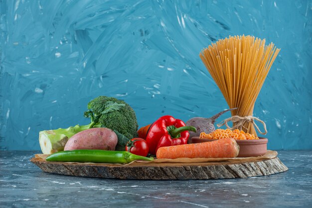 Gemüse auf einem Brett neben Spaghetti-Nudeln, auf dem Marmorhintergrund.