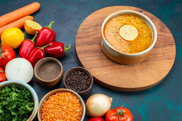 Gemüsesuppe mit halber Draufsicht mit frischem Gemüse, Gemüse und Gewürzen auf einem dunkelblauen Schreibtisch.