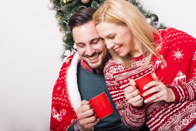 Gemütliche Aufnahme eines glücklichen Paares, das heißen Tee auf dem Hintergrund des Weihnachtsbaums trinkt?