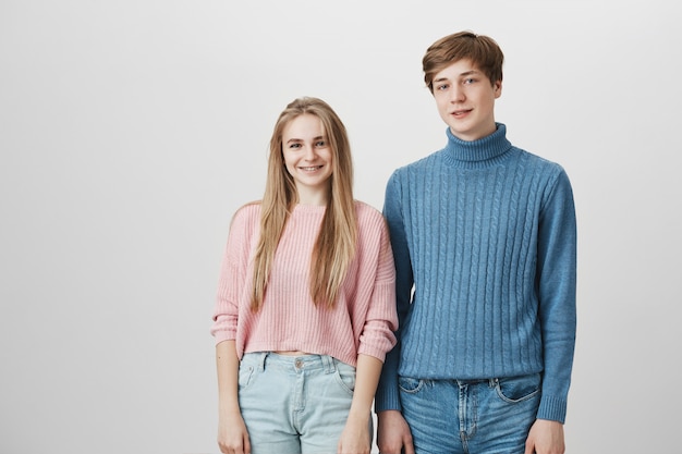 Gemütliche Aufnahme von kaukasischen Freunden, die gestrickte Pullover tragen, die drinnen aufwerfen. Hipster Kerl mit blonden Haaren und blauen Augen, die hinter seiner niedlichen blonden Freundin stehen