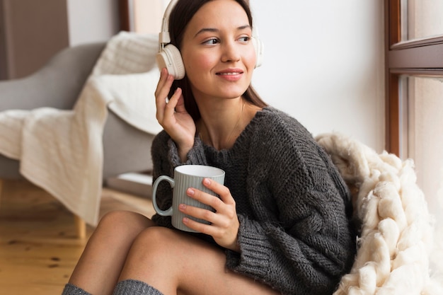 Gemütliche Frau des mittleren Schusses mit Becher, der Musik hört