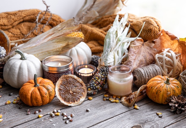 Gemütliche herbstliche Komposition mit Kerzen, Kürbissen, Mais auf einer Holzoberfläche im rustikalen Stil.