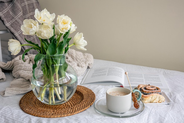 Gemütliche Komposition mit einem Blumenstrauß Kaffee und einem Brötchen im Bett