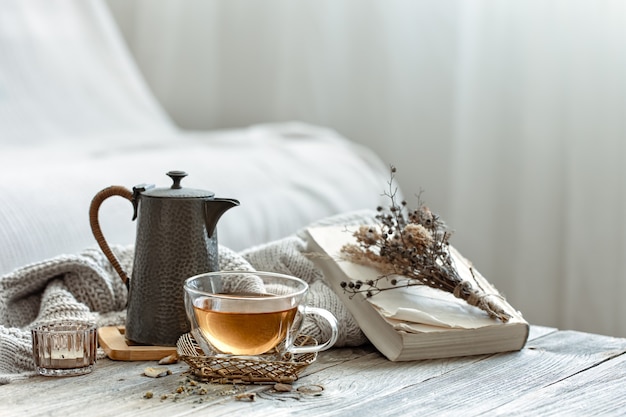 Gemütliche Komposition mit einer Tasse Tee und einem Buch im Inneren des Raumes auf unscharfem Hintergrund.